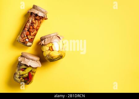Konserven und konserviertes Gemüse in Glasgefäßen über gelbem Hintergrund. Draufsicht. Flaches Lay. Kopierbereich Stockfoto