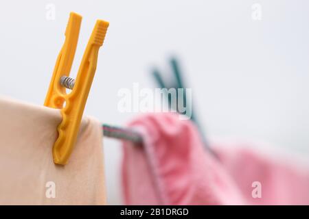 Beige und pinkfarbene Kleidung wird an einem Seil mit Kunststoffkleidern getrocknet. Stockfoto