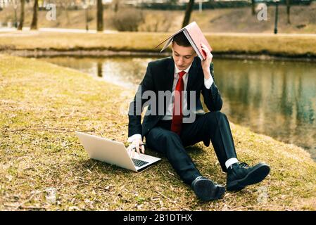 Junger Kerl müde von der Arbeit, Mann in einem Anzug, der auf der Natur in der Nähe des Sees läuft. Generationen Y, Millennials Stockfoto
