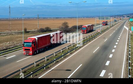 Rote Lkws in Reihe als Konvoi auf einer ländlichen Landstraße unter einem wunderschönen blauen Himmel Stockfoto