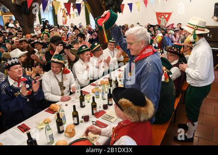 25. Februar 2020, Baden-Württemberg, Riedlingen: Winfried Kretschmann (Bündnis 90/die Grünen, vorne stehend), Ministerpräsident von Baden-Württemberg, grüßt am Schrove-Dienstag die Narren im Rathaus. Neben ihm sitzen Vize-Zunftmeister Lothar Sauter (l) und Ehrenzunftmeister Peter Bucher (r). Mehr als 300 Narren der Narrenzunft Gole 1865 nehmen am Zigarrenrauchen Teil, die 191. Froschtrippe isst und die folgende Rutsche aus dem Rathaus und will später durch die Stadt ziehen. Froschtrippe ist eine Riedlinger Spezialität. Es handelt sich um geschnittene, in Essig eingelegte Rinderstomachen. Foto: Felix Kästl Stockfoto