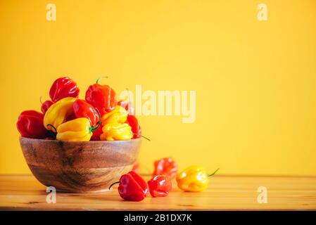 Bunte Chilischoten aus der Motorhaubenhaube in Holzschale über orangefarbenem Hintergrund. Kopierbereich Stockfoto