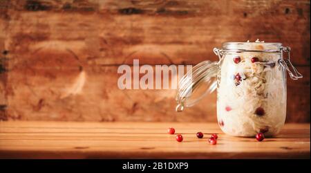 Fermentierter Kohl mit Preiselbeere im Glasbecher über Holzhintergrund. Probiotika Lebensmittelkonzept. Konservierte vegetarische Ernährung, hausgemachte Gärung. Banner mit Kopierbereich. Stockfoto
