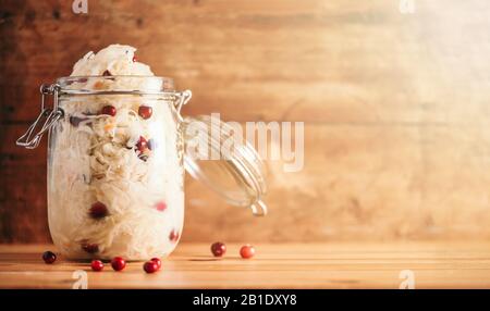 Fermentierter Kohl mit Preiselbeere im Glasbecher über Holzhintergrund. Probiotika Lebensmittelkonzept. Konservierte vegetarische Ernährung, hausgemachte Gärung. Banner mit Kopierbereich. Stockfoto