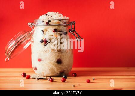 Fermentierter Kohl mit Preiselbeere im Glasbecher über Holz und rotem Hintergrund. Probiotika Lebensmittelkonzept. Konservierte vegetarische Ernährung, hausgemachte Gärung. Banner mit Kopierbereich. Stockfoto