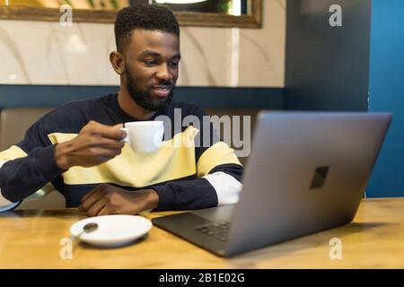 Profilporträt des jungen afrikanischen Webshop-Managers, indem er seinem Partner im Café eine Nachricht auf einem Laptop eingibt Stockfoto