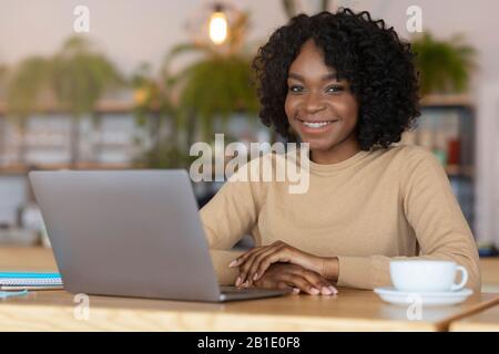 Afro Mädchen lächelt bei der Arbeit im Café an der Kamera Stockfoto