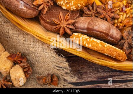 Plätzchen, Schokoladenkuchen, Bagels, Anissterne in einem Korbkorb auf dem Hintergrund rauer Homespun-Qualität. Nahaufnahme Stockfoto