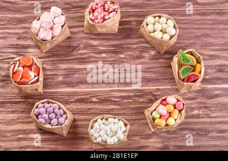 Papiertüte mit farbigen Marshmallows und Karamellkanschen auf einem Holztisch in der Draufsicht. Kopierbereich. Stockfoto