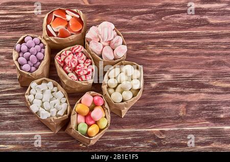 Papiertüte mit farbigen Marshmallows und Karamellkanschen auf einem Holztisch in der Draufsicht. Kopierbereich. Stockfoto