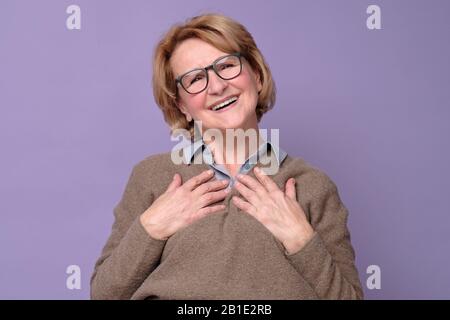 Die ältere lustige Frau erhält immer wieder Komplimente, die auf der Geburtstagsparty frisch und schön aussehen. Entzückende, charmante alte Dame, die Palmen am Herzen hält Stockfoto