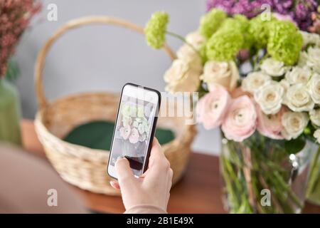 Eine Frau macht ein Foto auf ihrem Telefon mit Blumen. Blumengeschäft Konzept . Blumenfrau schafft Blumenarrangement in einem Korbkorb. . Blumen Lieferung. Stockfoto