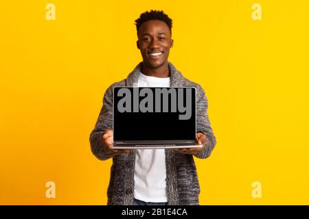 Junger freudiger afrikanischer Mann, der sich in den Händen hält, Laptop Stockfoto