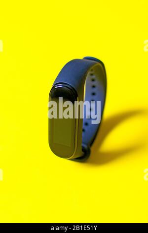 Klassischer blauer Fitness-Tracker auf hellgelbem Hintergrund. Fitness-Armband für Sporttraining. Gesunder Lebensstil. Stockfoto