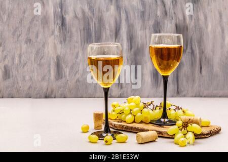 Weingläser, frische Trauben und Korken auf Holzhackbrett. Weinbar, Weingut, Weinverkostungskonzept. Hintergrund aus Steinbeton, Kopierraum Stockfoto