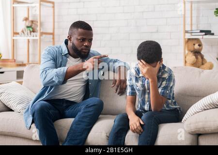 Wütender schwarzer Vater schimpft hartnäckigen Sohn wegen schlechten Verhaltens zu Hause Stockfoto