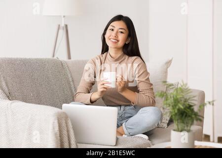 Viel Spaß am Wochenende. Asiatisches Mädchen entspannt, trinkt Kaffee und benutzt einen Laptop Stockfoto