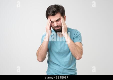 Besorgter junger Mann mit Kopfschmerzen, der die Hände an den Tempeln hält. Negative Gesichtsemotion. Stockfoto