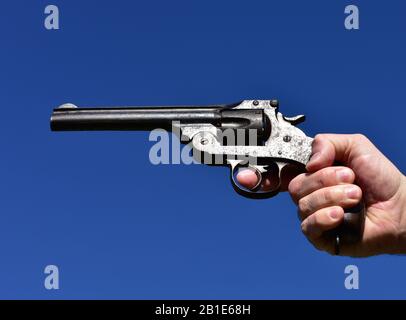 Mann, der einen Revolver im Kaliber .44 oder .45 im Freien mit blauem Himmel hält. Stockfoto