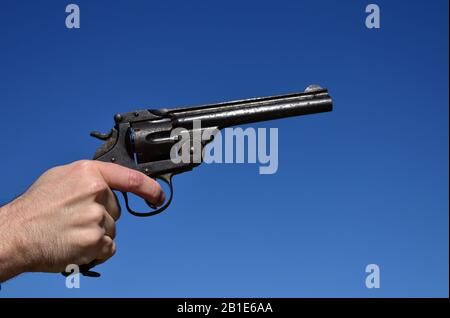 Mann, der einen Revolver im Kaliber .44 oder .45 im Freien mit blauem Himmel hält. Stockfoto