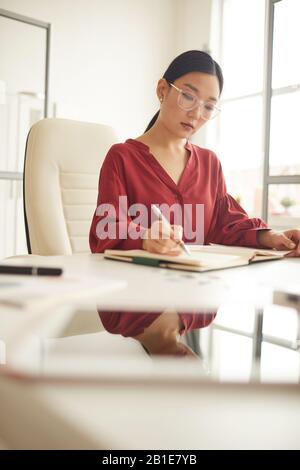 Vertikales Porträt eleganter Asiaten Lesen von Dokumenten am Schreibtisch im modernen weißen Büro, weibliches Chef-Konzept, Kopierraum Stockfoto