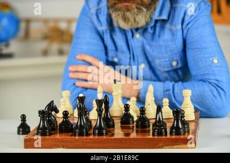 Schachfiguren auf Holzbrett. Fokussierter Schullehrer. Denken Sie daran, gegnerische Schachfiguren anzugreifen und einzufangen. Denken Sie an den nächsten Schritt. Bärtiger Mann trainiert für den Schachwettbewerb. Stockfoto