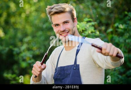 Hamburger kochen. Mann hält Grillausrüstung. Grillgut. Grillutensilien. Sommerwochenende. Werkzeuge zum Braten von Fleisch im Freien. Grillparty. Picknickkonzept. Grillchef. Gutaussehende Kerl, die Essen kochen. Stockfoto