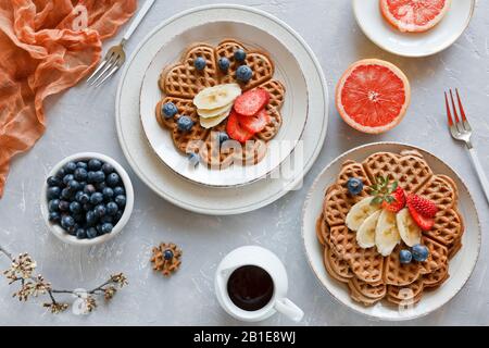 Stücke hausgemachter Waffelkuchen mit Bananen und Blaubeeren auf den Tellern auf grauem Grund Stockfoto