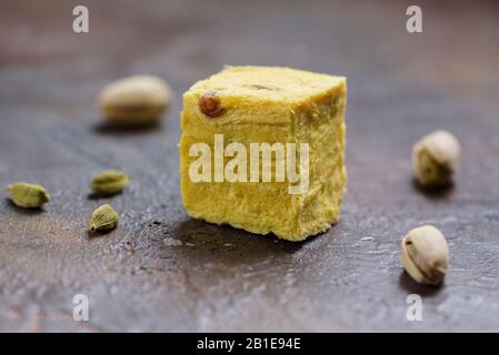 Ein Würfel aus Dessert soan Papdi, Kardamom-Körnern und Pistazien auf Betonküchenoberfläche. Stockfoto