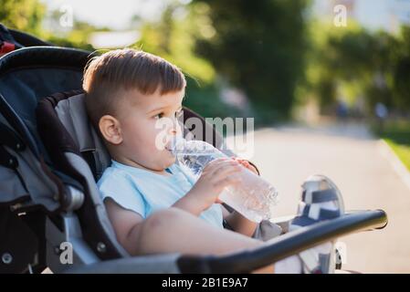 Cute Baby sitzt in einem Kinderwagen und Getränke sauberes Wasser und an einem heißen Sommertag Stockfoto