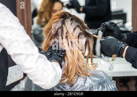 Friseur in schwarz Handschuhe ist färben die Haare einer Frau. Friseur ist die Farbe Creme im Haar. Malerei Haar. Stockfoto