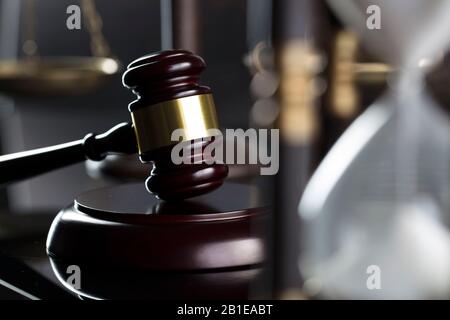 Gesetz- und Justizkonzept. Richtergavel, Sanduhr und Waage auf dem glänzenden, holzbraunen Tisch. Stockfoto