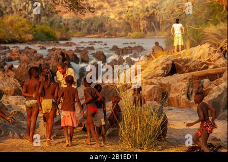 Europäische Frau gesellt sich mit Kindern des himba-stammes bei Epupa Falls, Kunene Region, in Namibia Stockfoto