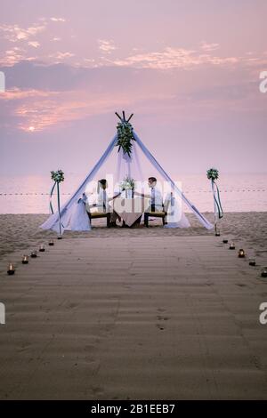 Junge Paare Flitterwochen-Abendessen bei Kerzenlicht bei Sonnenuntergang am Strand, Männer und Frauen Abendessen am Strand romantische Einstellung in Thailand Stockfoto