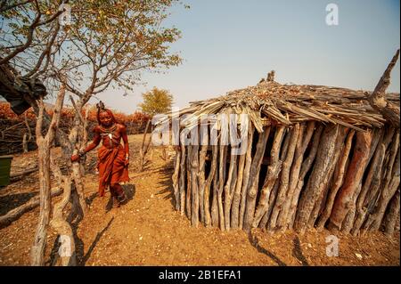 Himba-Frau mit traditioneller Kleidung in der Nähe seiner primitiven Hütte in seinem Dorf in der Nähe der Epupa-Fälle, in Namibia Stockfoto