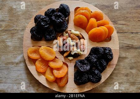 Getrocknete Aprikosen, Pflaumen und Nuss vermischen sich auf verwittertem Holzhintergrund. Stockfoto