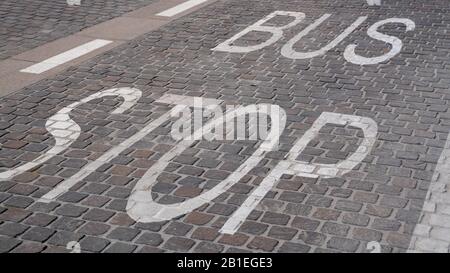 Auf den Fliesen auf der Straße ist das Schild mit der Bushaltestelle in weißer Farbe gestrichen. Stockfoto