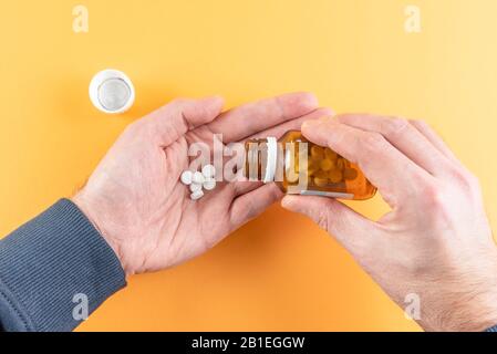 Person, die Pillen oder Tabletten aus der Pillenflasche vor orangefarbenem Hintergrund gießt Stockfoto