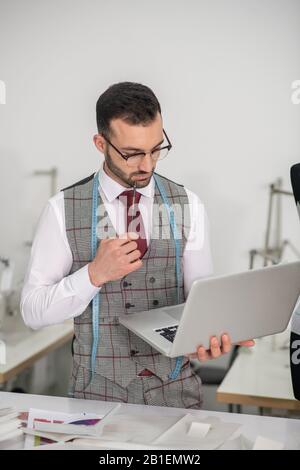 Schneiderstecker hält Laptop in einer Hand und Bleistift in einer anderen Stockfoto