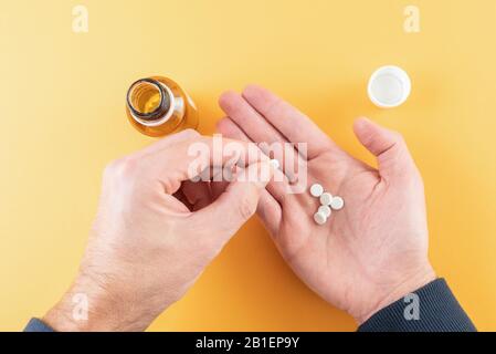 Medikationstabletten in Handfläche vor orangefarbenem Hintergrund mit Pillenflasche Stockfoto