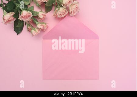 Hochzeit oder Geburtstag verspotten. Leerer offener Umschlag mit Platz für Text für die Grußkarte der Feder. Blumenstrauß aus rosa Rosen auf pinkfarbenem Hintergrund. Flach Stockfoto