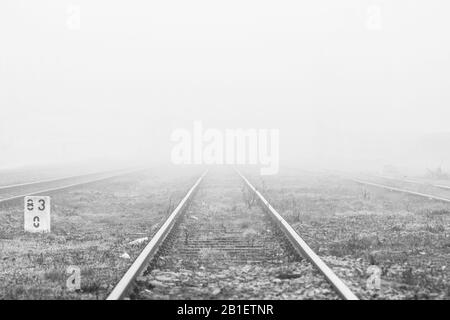Die Perspektive der Bahngleise verschwindet in Nebel am nebligen Morgen - monochromes Bild Stockfoto