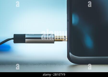 Anschluss der 3,5-mm-Audiobuchse an ein schwarzes Mobiltelefon. Stockfoto