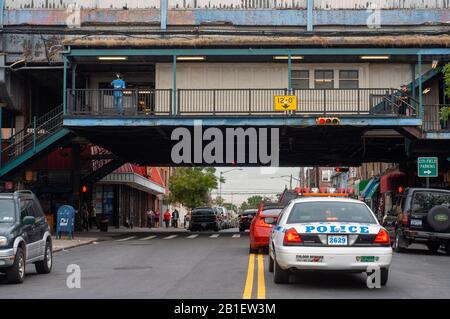 Autos und Polizeiwagen fahren auf Nothtern bulevard Queens unter der U-Bahn Stockfoto