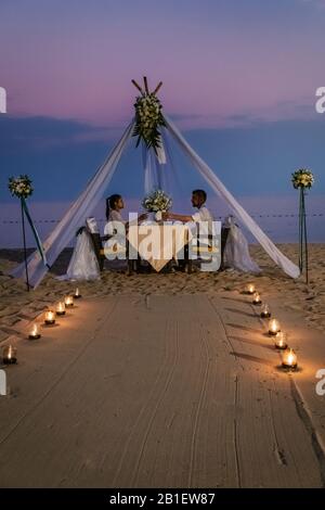 Junge Paare Flitterwochen-Abendessen bei Kerzenlicht bei Sonnenuntergang am Strand, Männer und Frauen Abendessen am Strand romantische Einstellung in Thailand Stockfoto