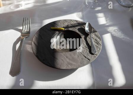 Leerer schwarzer Teller in einem Restaurant, nach Gourmet-Essen, Löffelgabel auf dem Tisch Stockfoto