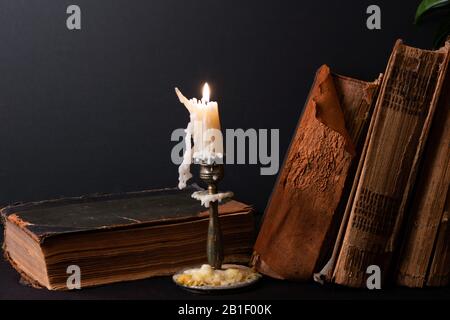 Stapel alter Bücher mit vergilbten Schabbseiten und Kerzenleuchter mit brennenden Kerzen Stockfoto