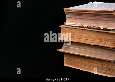 Stapel alter Bücher mit vergilbten Schabbseiten, die auf schwarzem Stoff liegen Stockfoto