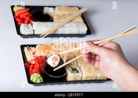 Sushi mit Stöcken aus Plastick Boxen auf weißem Hintergrund essen. Stockfoto