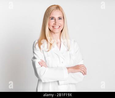 Fröhliche Frau mittleren Alters, Ärztin in gleichförmigen Kreuzarmen Stockfoto